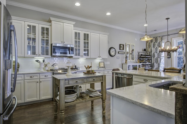 kitchen with white cabinetry, appliances with stainless steel finishes, ornamental molding, and pendant lighting