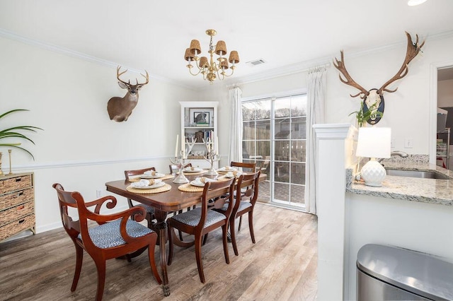 dining area with an inviting chandelier, light wood-style flooring, visible vents, and ornamental molding