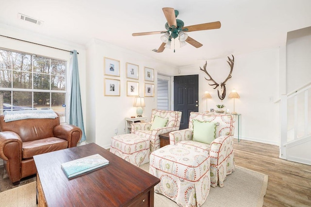 living room with crown molding, visible vents, ceiling fan, wood finished floors, and baseboards