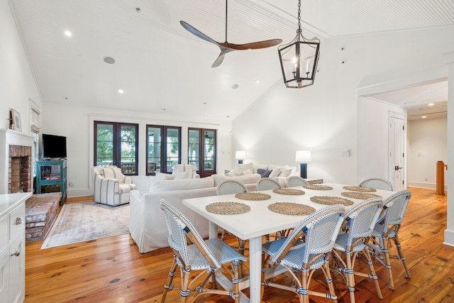 dining space featuring light hardwood / wood-style floors, vaulted ceiling, ceiling fan with notable chandelier, a fireplace, and ornamental molding