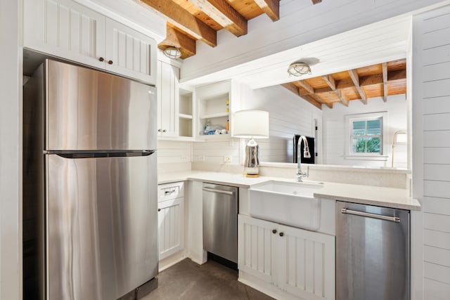 kitchen featuring white cabinets, beamed ceiling, stainless steel appliances, wooden walls, and sink