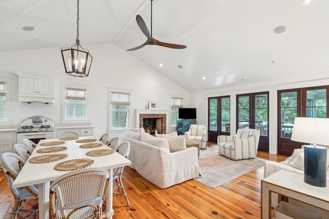 living room with ceiling fan with notable chandelier, light wood-type flooring, a fireplace, and high vaulted ceiling