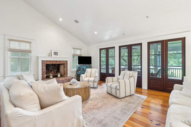 living room with light hardwood / wood-style floors, a brick fireplace, french doors, and high vaulted ceiling