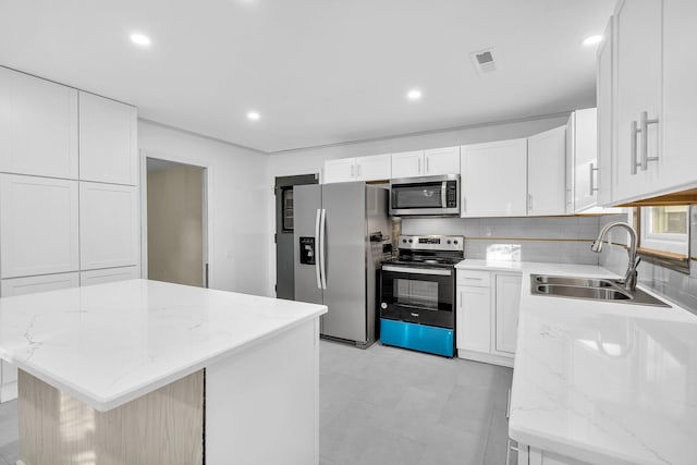 kitchen featuring sink, a kitchen island, light stone counters, white cabinets, and appliances with stainless steel finishes