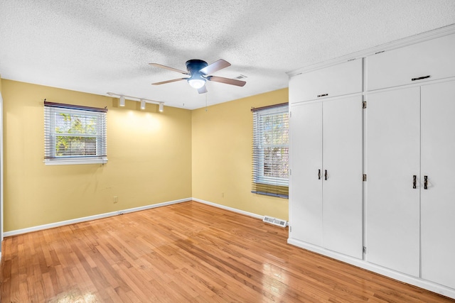 unfurnished bedroom with a textured ceiling, light wood-type flooring, rail lighting, and ceiling fan