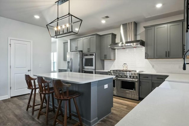 kitchen with wall chimney range hood, dark hardwood / wood-style flooring, decorative light fixtures, gray cabinets, and appliances with stainless steel finishes