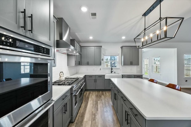 kitchen with stainless steel appliances, sink, wall chimney range hood, a center island, and gray cabinets