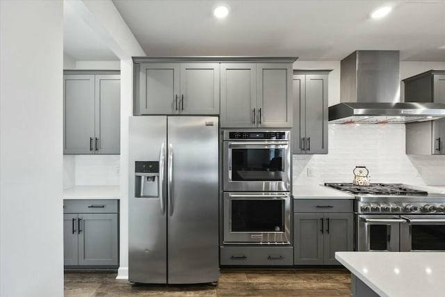 kitchen featuring decorative backsplash, appliances with stainless steel finishes, wall chimney exhaust hood, and gray cabinetry