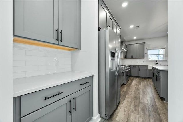 kitchen featuring gray cabinetry, sink, wall chimney exhaust hood, appliances with stainless steel finishes, and light wood-type flooring