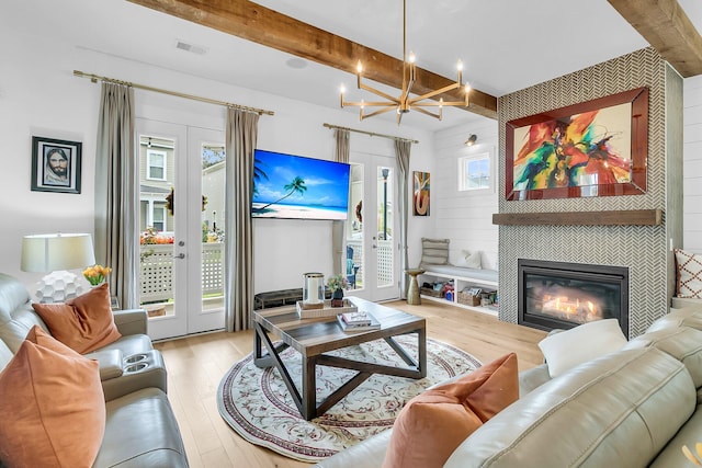 living room with light hardwood / wood-style floors, beamed ceiling, a tile fireplace, an inviting chandelier, and french doors