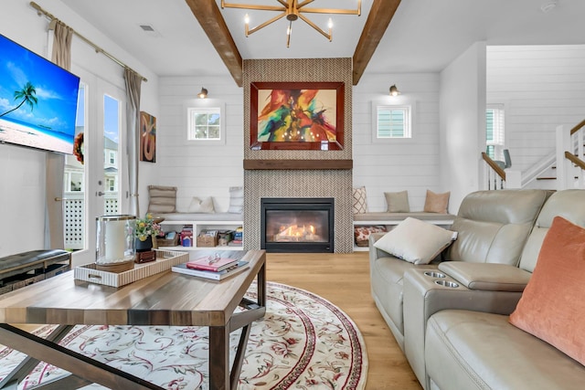 living room featuring light hardwood / wood-style flooring, beam ceiling, a tiled fireplace, and a healthy amount of sunlight