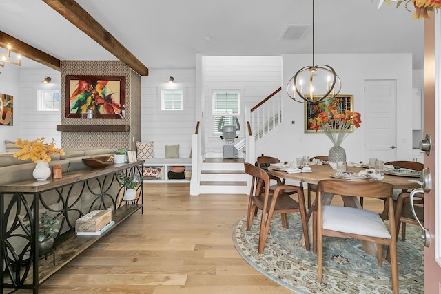 dining space featuring light hardwood / wood-style flooring, wood walls, a notable chandelier, and beamed ceiling