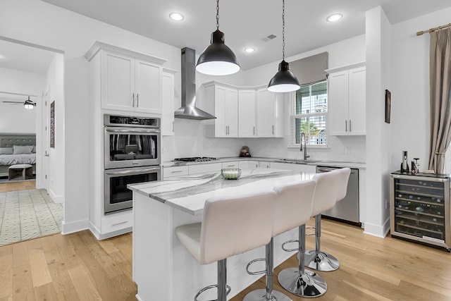 kitchen with sink, white cabinetry, a kitchen island, wall chimney range hood, and appliances with stainless steel finishes