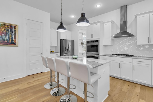 kitchen featuring appliances with stainless steel finishes, wall chimney exhaust hood, white cabinetry, and light hardwood / wood-style floors