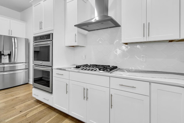 kitchen featuring light hardwood / wood-style floors, white cabinets, wall chimney exhaust hood, appliances with stainless steel finishes, and light stone countertops