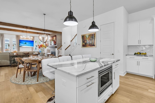 kitchen with light hardwood / wood-style floors, stainless steel microwave, a breakfast bar area, and white cabinets