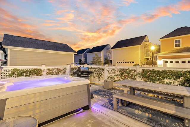 patio terrace at dusk with a wooden deck, a hot tub, grilling area, and a garage