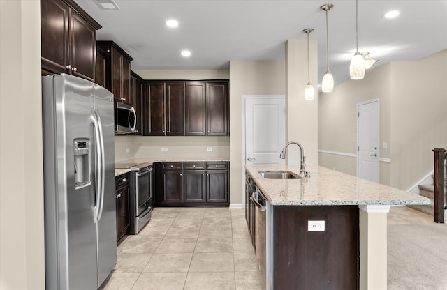 kitchen with sink, appliances with stainless steel finishes, hanging light fixtures, light stone countertops, and a center island with sink