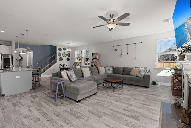 living room with light wood-type flooring and ceiling fan with notable chandelier