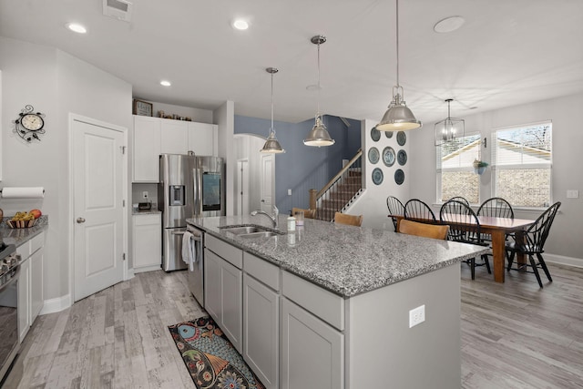 kitchen with pendant lighting, stainless steel appliances, an island with sink, sink, and light wood-type flooring