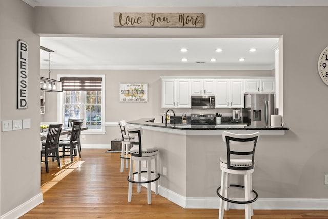 kitchen with white cabinets, appliances with stainless steel finishes, a kitchen breakfast bar, hanging light fixtures, and kitchen peninsula