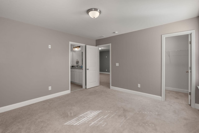 unfurnished bedroom with light colored carpet, ensuite bathroom, a closet, and a walk in closet