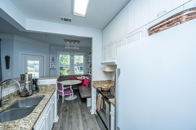 kitchen with a sink, visible vents, white cabinets, freestanding refrigerator, and stainless steel range with electric stovetop