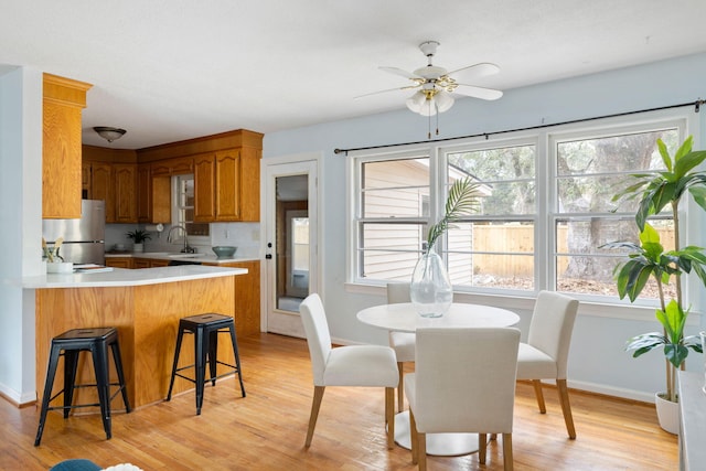 kitchen with light countertops, brown cabinets, a peninsula, freestanding refrigerator, and a sink