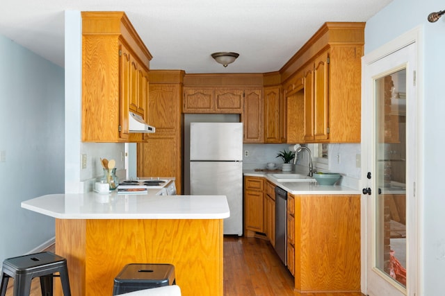 kitchen with a sink, under cabinet range hood, appliances with stainless steel finishes, a peninsula, and light countertops