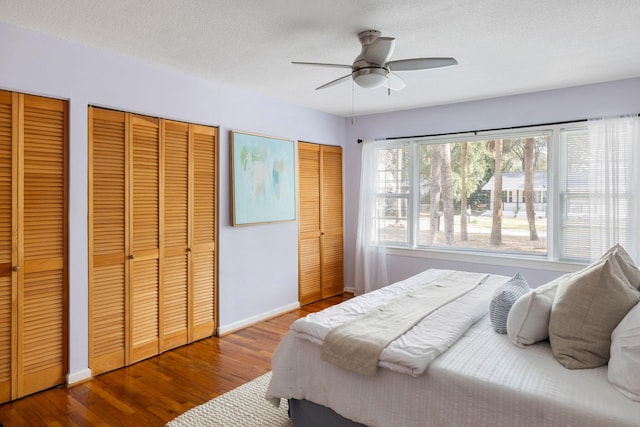 bedroom with two closets, baseboards, wood finished floors, a textured ceiling, and a ceiling fan