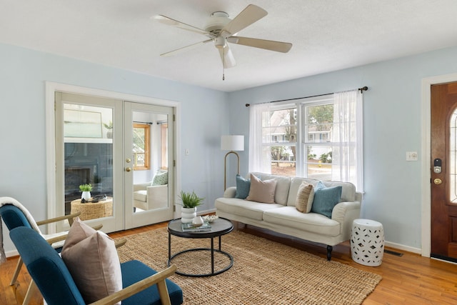 living area featuring a ceiling fan, visible vents, baseboards, light wood-style flooring, and french doors