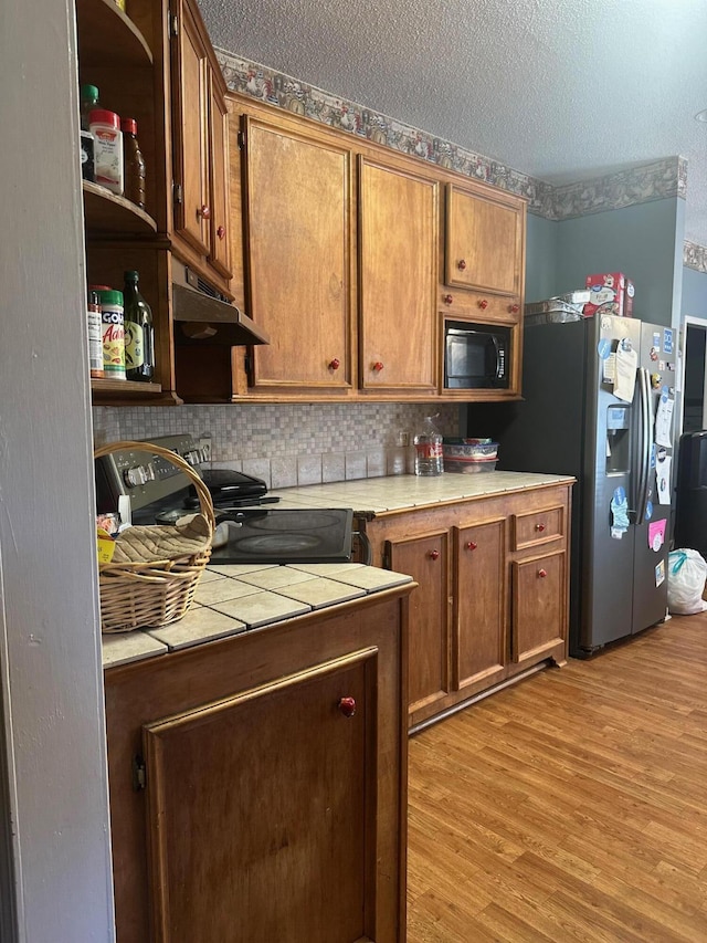 kitchen featuring black appliances, decorative backsplash, a textured ceiling, tile counters, and light hardwood / wood-style floors