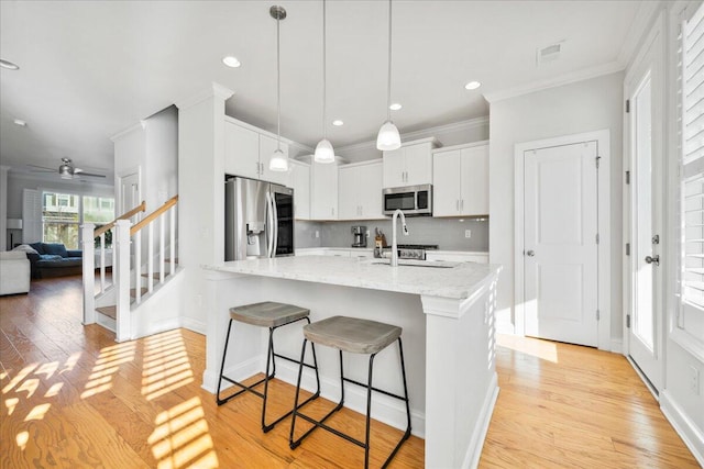 kitchen featuring a breakfast bar area, light stone countertops, stainless steel appliances, light wood-type flooring, and white cabinetry