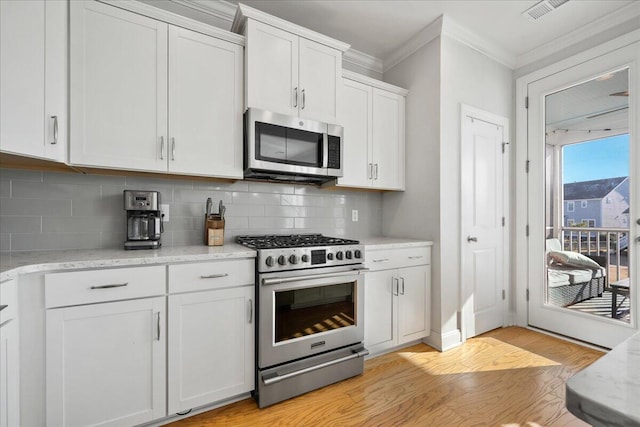 kitchen featuring crown molding, light wood finished floors, stainless steel appliances, tasteful backsplash, and white cabinetry