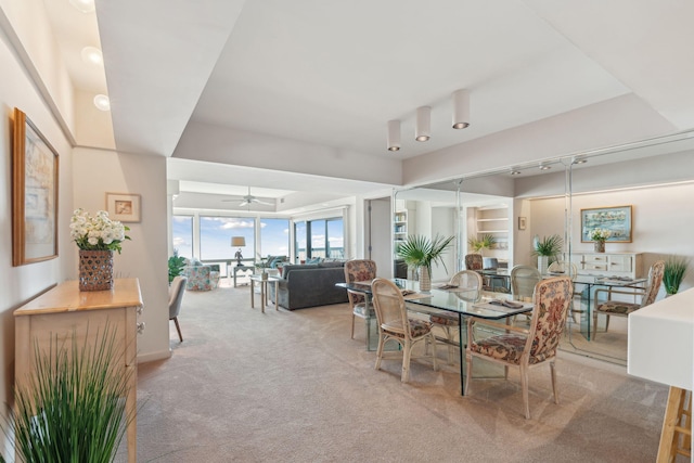 dining area with ceiling fan, a raised ceiling, rail lighting, and light colored carpet