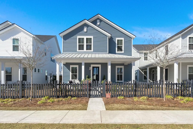 traditional-style house with a fenced front yard, covered porch, metal roof, and a standing seam roof