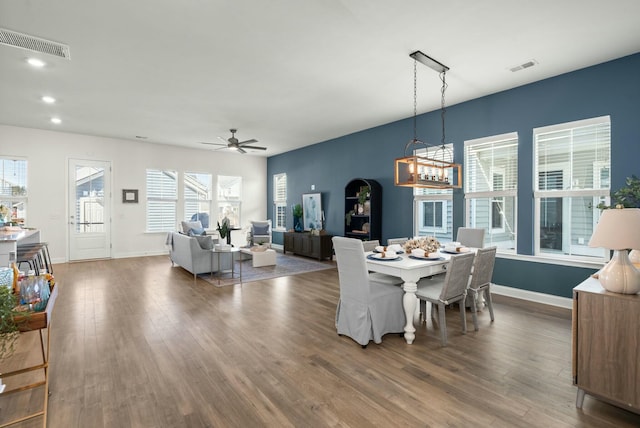 dining room featuring baseboards, visible vents, wood finished floors, and ceiling fan with notable chandelier