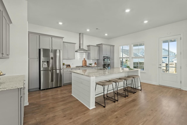 kitchen featuring dark wood-style floors, stainless steel appliances, gray cabinets, decorative backsplash, and wall chimney exhaust hood