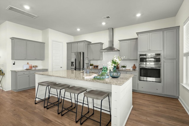 kitchen with stainless steel appliances, wall chimney range hood, gray cabinets, and visible vents