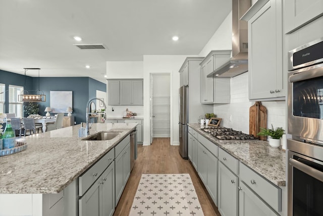 kitchen featuring visible vents, gray cabinets, stainless steel appliances, wall chimney range hood, and a sink