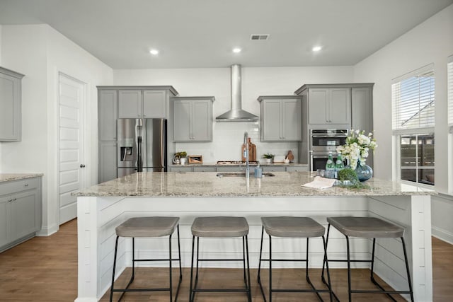 kitchen featuring a breakfast bar, visible vents, appliances with stainless steel finishes, gray cabinets, and wall chimney exhaust hood