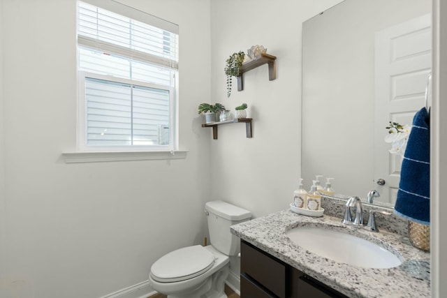 half bathroom with a healthy amount of sunlight, baseboards, toilet, and vanity