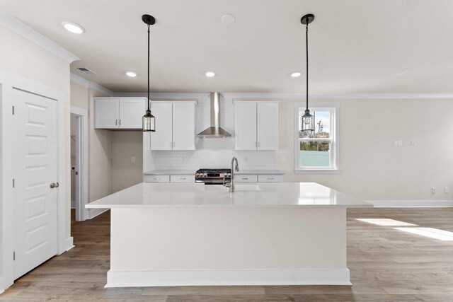 kitchen with decorative light fixtures, an island with sink, light wood-type flooring, and wall chimney exhaust hood