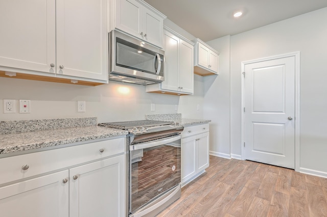 kitchen featuring white cabinets, light wood-type flooring, appliances with stainless steel finishes, and light stone counters