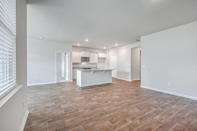 kitchen with hardwood / wood-style flooring, a kitchen breakfast bar, white cabinetry, and a kitchen island with sink