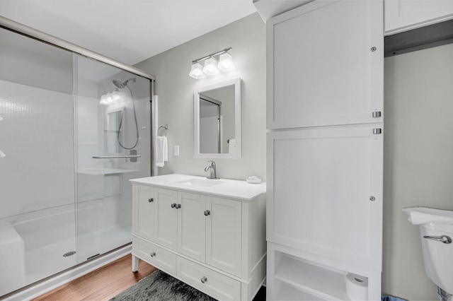 bathroom featuring toilet, wood finished floors, a shower stall, and vanity