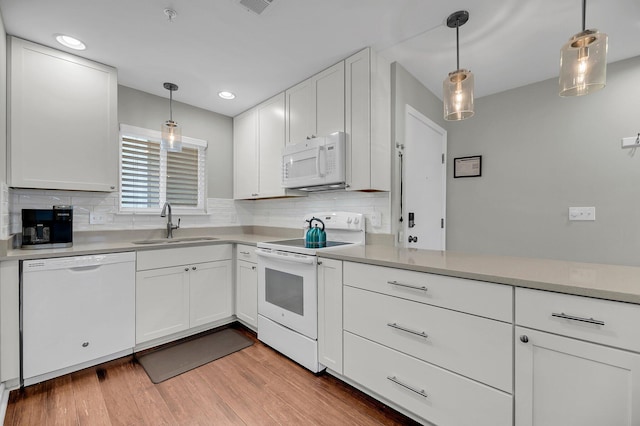 kitchen featuring white appliances, hanging light fixtures, light countertops, white cabinetry, and a sink