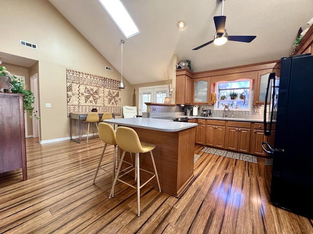 kitchen featuring black refrigerator, a kitchen breakfast bar, backsplash, kitchen peninsula, and light hardwood / wood-style flooring