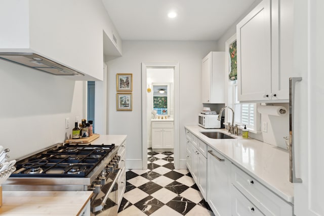 kitchen featuring range hood, white cabinetry, range with two ovens, and sink