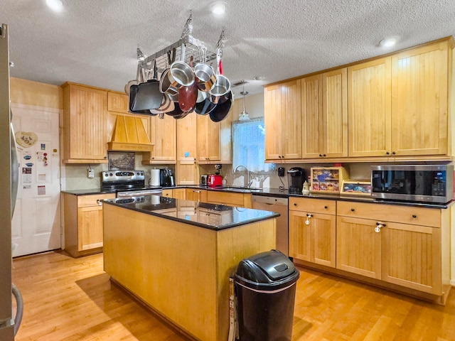 kitchen featuring appliances with stainless steel finishes, custom range hood, sink, light hardwood / wood-style flooring, and a center island